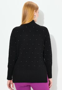 Svart stickad tröja med diamantmönster och små silverdetaljer, ribbad nederkant och krage, med avslappnad passform och långa ärmar.