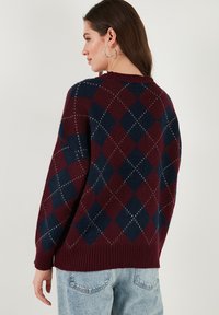 Pull en motif argyle bordeaux et marine avec un ourlet côtelé, présentant une coupe décontractée et une texture douce. Des détails de couture visibles mettent en valeur le design.