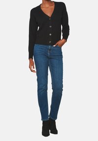 Black cardigan with a v-neckline, front button closure, and long sleeves, paired with blue slim-fit jeans and black ankle boots.