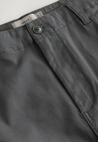 Pantalon gris en coton avec fermeture à boutons, passants de ceinture, et une étiquette de marque "NEXT" visible sur la ceinture intérieure.