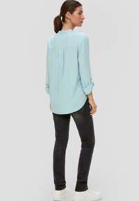 Hellblaue Langarmbluse mit abgerundetem Saum, Rückenfalte, aufgerolltenÄrmeln, kombiniert mit dunklen Jeans und weißen chunky Sneakers.