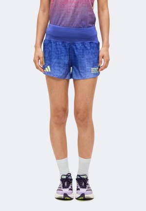 Personne portant un short de course Adidas bleu avec le logo du BMW Berlin Marathon, des chaussettes blanches et des chaussures de course violettes, debout, face à l'avant.