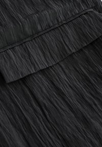 Černá tkanina s mačkanou texturou a vrstveným designem. Má volánkový okraj a hladký povrch, který zdůrazňuje plynulost materiálu.
