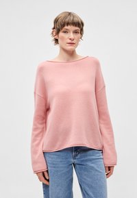 Camisa de malha cor-de-rosa clara com decote amplo em barco, mangas compridas e corte descontraído, combinada com jeans azul. Textura suave e design casual.