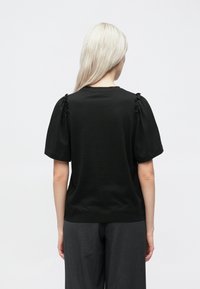 Fekete, rövid ujjú felső, laza szabással. Ráncolt részletekkel a vállvarrásoknál. Simogató tapintású, klasszikus kerek kivágású.