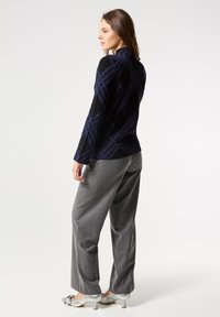 Blazer negro y azul con estampado, fabricado en tejido texturizado, diseño ajustado y mangas largas, combinado con pantalones de pierna ancha en gris y zapatos plateados.