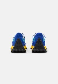 Blue suede sneakers with yellow rubber soles and black textured outsoles. Features a triangular design and light blue accents on the sides.