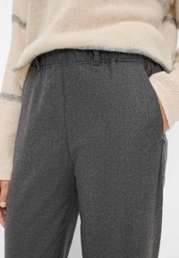 Graue maßgeschneiderte Hose aus strukturiertem Stoff, mit einem elastischen Bund und Seitentaschen, kombiniert mit einem creme- und graustreifen Pullover.