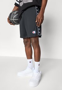 Sorte idrettsshorts med side-striper som har Champion-logoen, hvite sportssokker og hvite joggesko. Basketballen har en strukturert overflate.