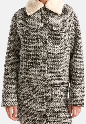 Mustavalkoinen tweedtakki mustilla nappeilla ja kermaisella karvakauluksella, yhdistettynä vastaavaan tweedhameeseen, jossa napit edessä.