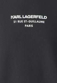 Logo Karla Lagerfelda s textem "21 Rue St-Guillaume Paříž" tištěným bílou barvou na černém tkanivu.