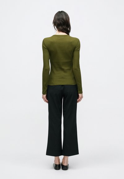 Μπλούζα με μακριά μανίκια, εφαρμοστή, με ριμπ ύφανση σε ελιά πράσινο, σε συνδυασμό με παντελόνια φαρδιά μαύρα. Μονόχρωμα, λεία υφή, λιτές λεπτομέρειες.