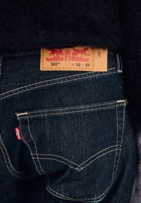 Close-up of dark blue denim jeans back pocket with red Levi's label and leather patch showing size W32 L32.
