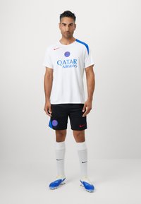 Hvid atletisk skjorte med blå detaljer, mærket med "Qatar Airways" logo, parret med sorte shorts, hvide sokker og blå fodboldstøvler.