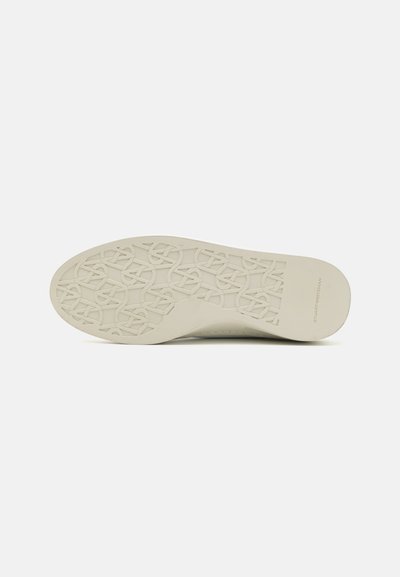 Suela de zapato en goma color blanco roto con un patrón texturizado que presenta diseños entrelazados y el logotipo de la marca. Acabado suave y borde del tacón redondeado.