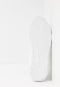 Suola di scarpa bianca in gomma testurizzata, con scanalature orizzontali e un delicato marchio impresso. La forma curvata sottolinea il supporto per il piede.