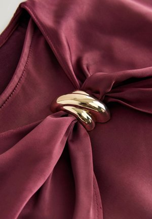 Burgunderfarbener Satin-Stoff mit glatter Oberfläche, versehen mit einem verdrehten goldenen Metallakzent am Knoten. Schlankes und elegantes Design.