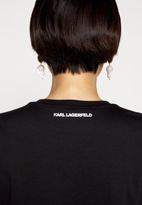 Camiseta negra con el logo blanco de "KARL LAGERFELD" en la parte de atrás, de mangas cortas, cuello redondo y textura de tela suave.