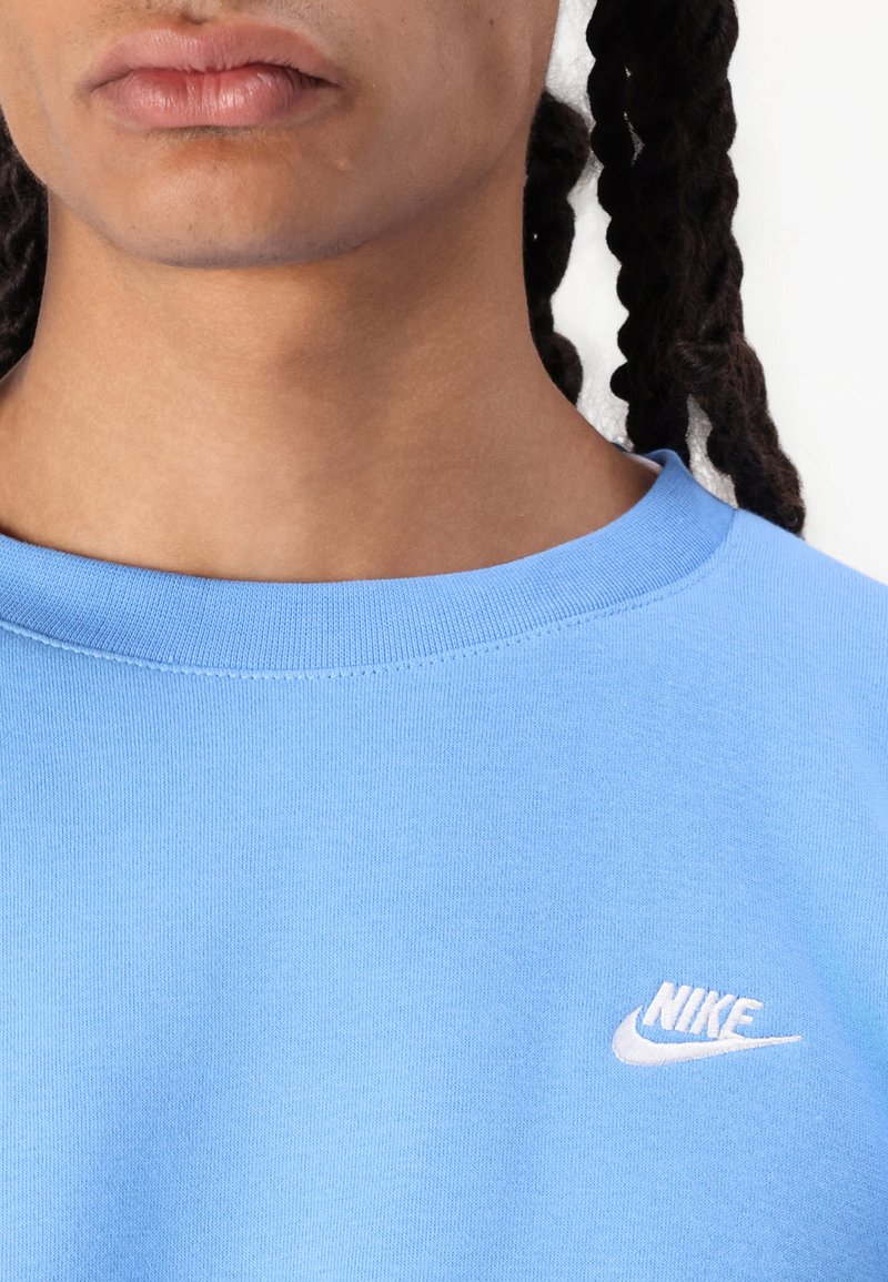 Lichtblauw Nike sweatshirt met een ronde hals. Kenmerkt zich door een witte geborduurde logo op de linker borst. Zachte textuur, normale pasvorm.