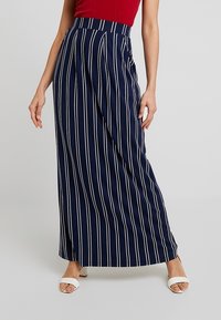 Navy gestreepte maxi rok met witte verticale lijnen, geplooid ontwerp, hoge taille, gemaakt van zachte stof, gecombineerd met witte sandalen.