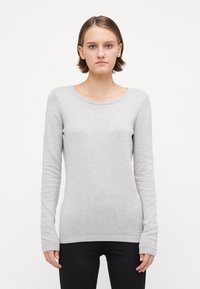 Pulover lung cu mâneci lungi de culoare gri deschis, cu un model texturat și un decolteu cu bordură. Croială slim, cu manșete strânse, purtat cu pantaloni negri.