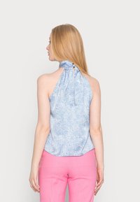 Top sin mangas de color azul claro con cuello alto, presenta un patrón texturizado y pequeño cierre de botón en la parte posterior. Combinado con pantalones rosas.