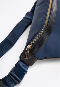 Námornícká crossbody taška vyrobená z nylonu s hladkou texturou, zlatým zipem a černými koženými detaily; nastavitelné ramínko s plastovou sponou.