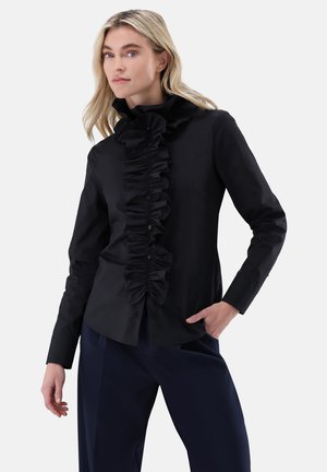 Black shirt with ruffled front detail, long sleeves, and buttons, made of smooth fabric. Paired with navy pants and featuring a high collar.