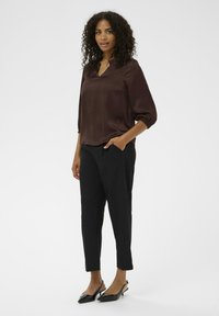 Blusa de satén marrón con escote en V y mangas tres cuartos, combinada con pantalones negros ajustados y zapatos de tacón negros y puntiagudos.
