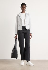 Light gray blazer with striped collar, white buttons, and side accents, paired with a white top, black wide-leg jeans, and white sneakers.