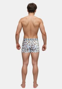 Herren-Boxershorts aus einem weißen Stoff mit Leopardenmuster, dekoriert mit einem schwarzen elastischen Bund, auf dem "KOUKOU" steht.