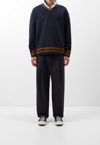 Marinblå tröja med orange och brun randig fåll, v-ringad design. Kombinerad med löst sittande mörka byxor och svarta sneakers.