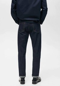 Mørke denim jeans med lige ben, med kontrastsyninger, to baglommer og opbrettede cuffs, parret med sorte sko.