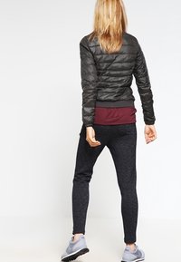 Svart puffjacka med horisontella sömmar, vinröd långärmad tröja under, mörka leggings och grå sportskor.