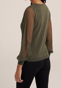 Olivgrön stickad tröja med transparenta randiga ärmar. Åtsittande design med ribbade mudd- och nederkanter som visar på kontrast i textur.