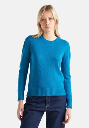 Hellblauer, gestrickter Pullover mit rundem Halsausschnitt, gerippten Bündchen und Saum. Glatte Textur und reguläre Passform. Kombiniert mit dunkler Jeans.