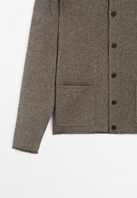 Grå stickad cardigan med knappframsidan, långa ärmar och två framfickor. Har ett texturerat tyg och svarta knappar.