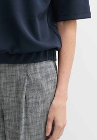 Top blu navy a maniche corte con vestibilità rilassata abbinato a pantaloni grigi con texture, caratterizzati da un motivo a gorripolo e pieghe frontali.