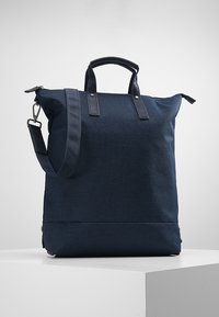 Bolso tote de color azul marino fabricado con tejido duradero, con acentos de cuero, asas dobles y una correa para el hombro desmontable. Diseño simple y rectangular.