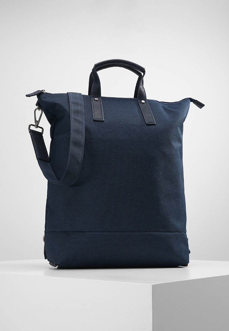 Bolso tote de color azul marino fabricado con tejido duradero, con acentos de cuero, asas dobles y una correa para el hombro desmontable. Diseño simple y rectangular.