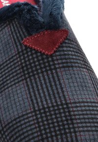 Superficie textil de cuadros en azul oscuro y negro con acentos rojos. Presenta un borde acolchado y un parche triangular burdeos con costura en zigzag.