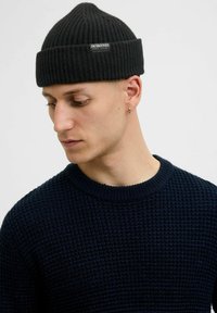 Gorro negro de canalé con una pequeña etiqueta, combinado con un suéter de textura azul marino con escote redondo. Tejido suave con un ajuste ceñido.