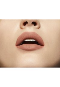 Rouge à lèvres nude mat sur des lèvres pleines, montrant une texture crémeuse. La peau est lisse avec un fini naturel, mettant en valeur la couleur des lèvres.