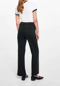 Jeans neri a vita alta e gamba larga con una texture liscia, dotati di tasche posteriori e gamba leggermente affusolata. Abbinati a una camicia bianca.