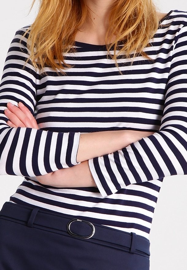 Haut à rayures bleu marine et blanc à manches longues avec un col rond. Le tissu est doux et présente une coupe ajustée. Une ceinture sombre est visible à la taille.