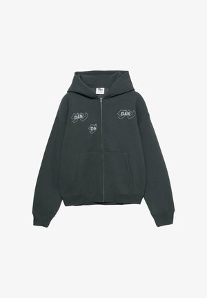 Sweat à capuche zippé vert foncé en tissu doux. Il comporte une grande poche avant et des imprimés graphiques blancs sur la poitrine et les manches.