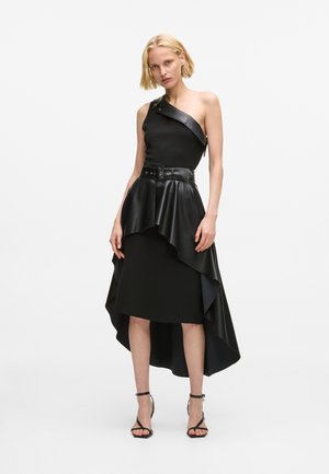 Czarna sukienka na jedno ramię z asymetrycznym warstwowym dołem, z paskiem w talii, wykonana z gładkiego, teksturowanego materiału.