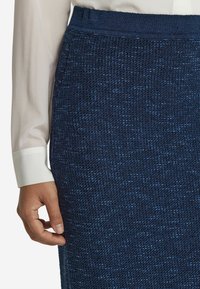 Marinblå vävd kjol med en strukturerad yta, med ett åtsittande midjeband och sidofickor. I sällskap med en vit långärmad blus.