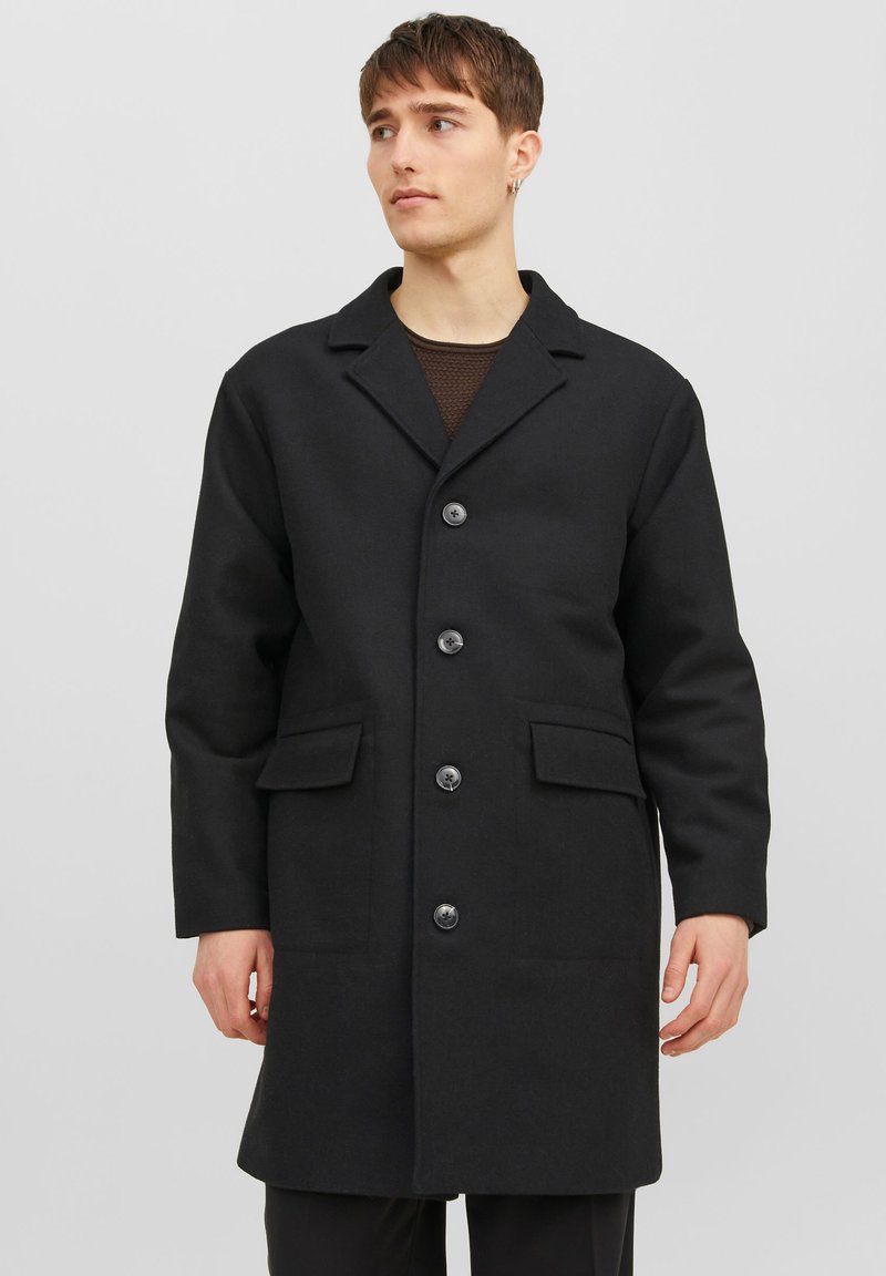 Svart ullkappa med slagkrage, sex knappar fram och två framfickor. Slät textur och skräddarsydd passform.