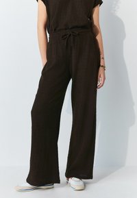 Zwarte, gestructureerde wijde broek met een elastische tailleband en trekkoord, voorzien van zijzakken en een relaxte pasvorm, gecombineerd met witte sneakers.